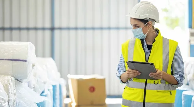 Warehouse worker in a mask with a tablet