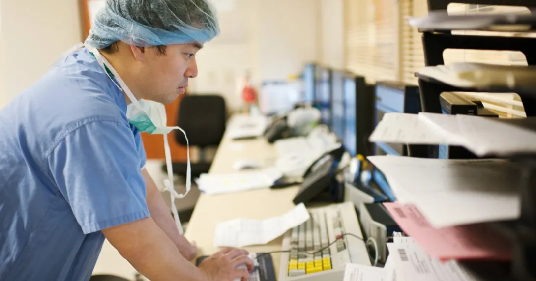 A clinician in scrubs looking at a computer A clinician in scrubs looking at a computer