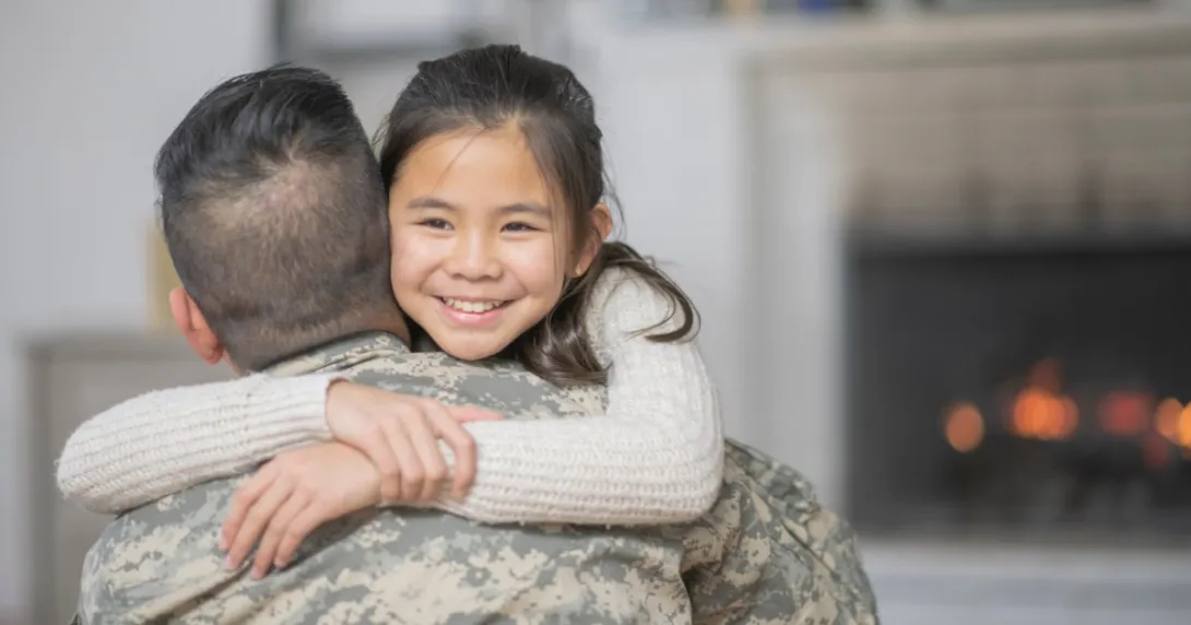 A person wearing military fatigues hugs a child.
