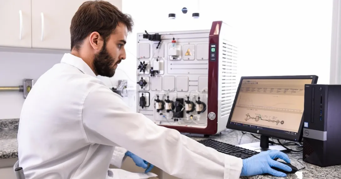A person in lab wear sits at a computer