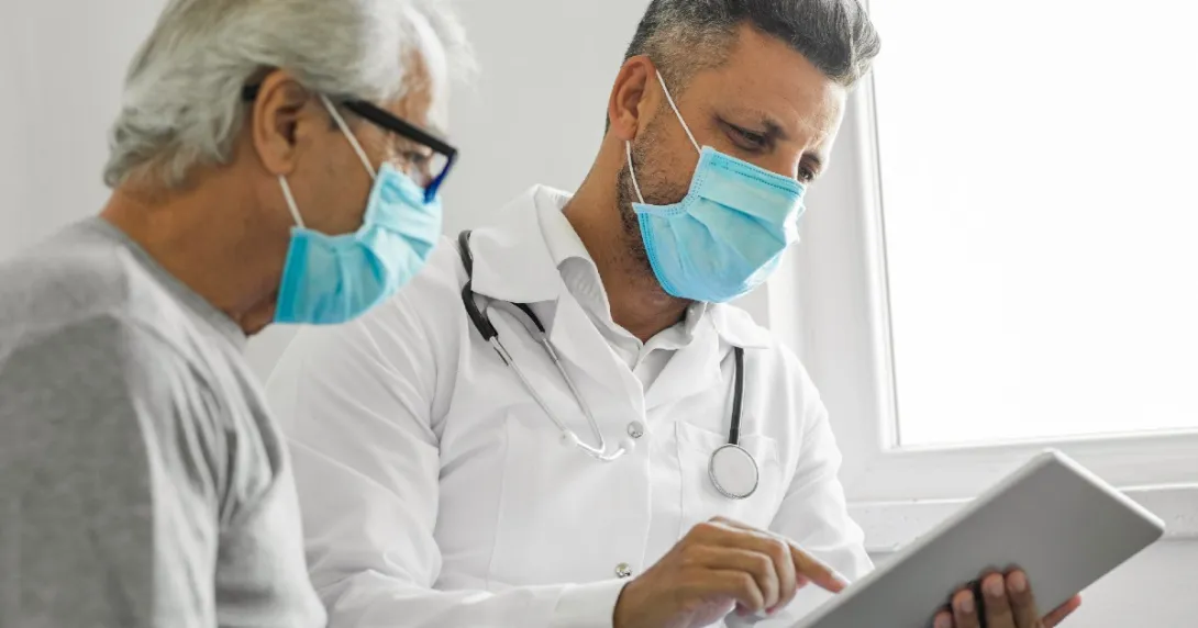 A doctor looks at a tablet with a patient looking over his shoulder