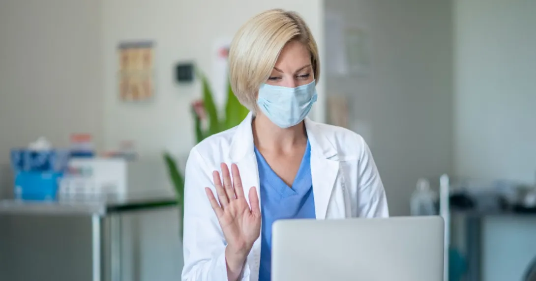 A doctor waves at a patient via telehealth