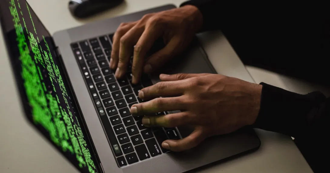 Hands work at a laptop showing code onscreen. Hands work at a laptop showing code onscreen.