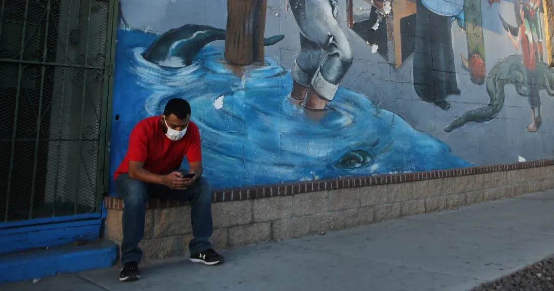A person in a mask sits looking at their phone