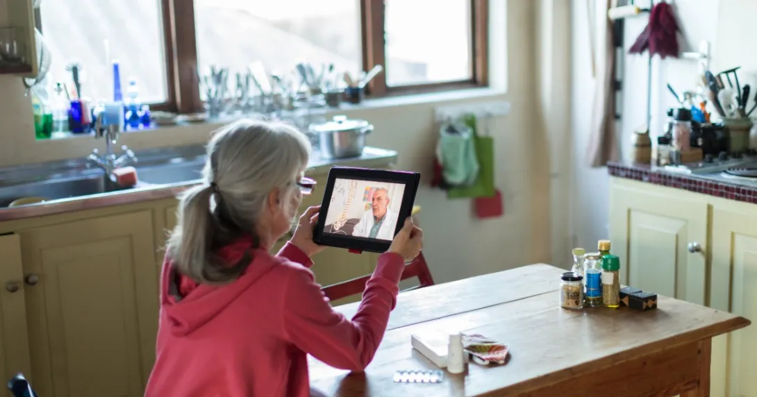 A person sits at a table speaking with a doctor via tablet.