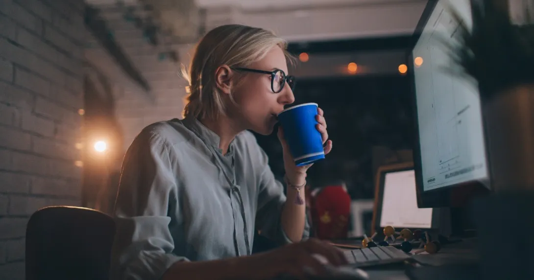 A person drinking coffee in front of a computer screen