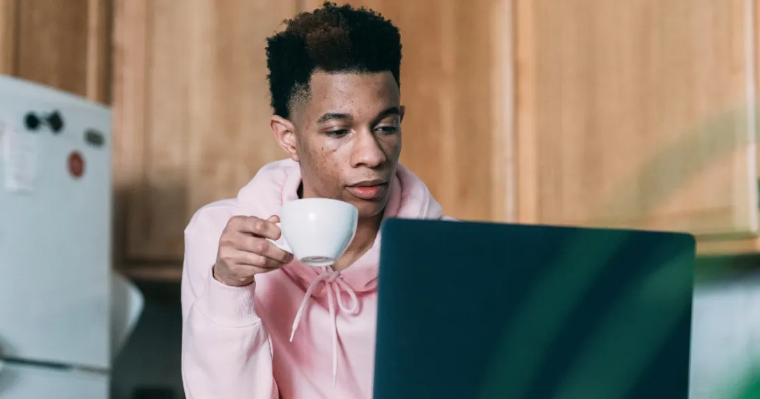 A person using a computer and holding a teacup