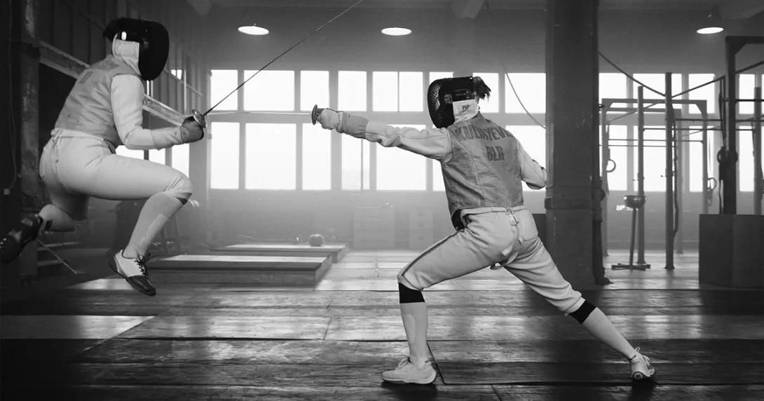 Black and white image of two individuals fencing. Black and white image of two individuals fencing. One is jumping but the opponent finds the weak spot.