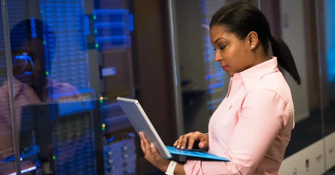 A person on a laptop in front of a server room