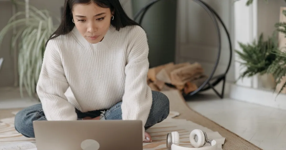 A laptop user in sweater and jeans sitting on the carpet