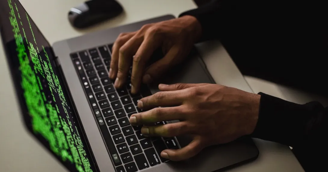 Hands are typing on a laptop with code on the screen.