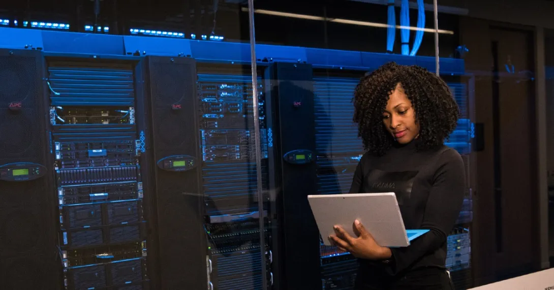 HIT professional reviews information on a laptop outside a server room HIT professional reviews information on a laptop outside a server room