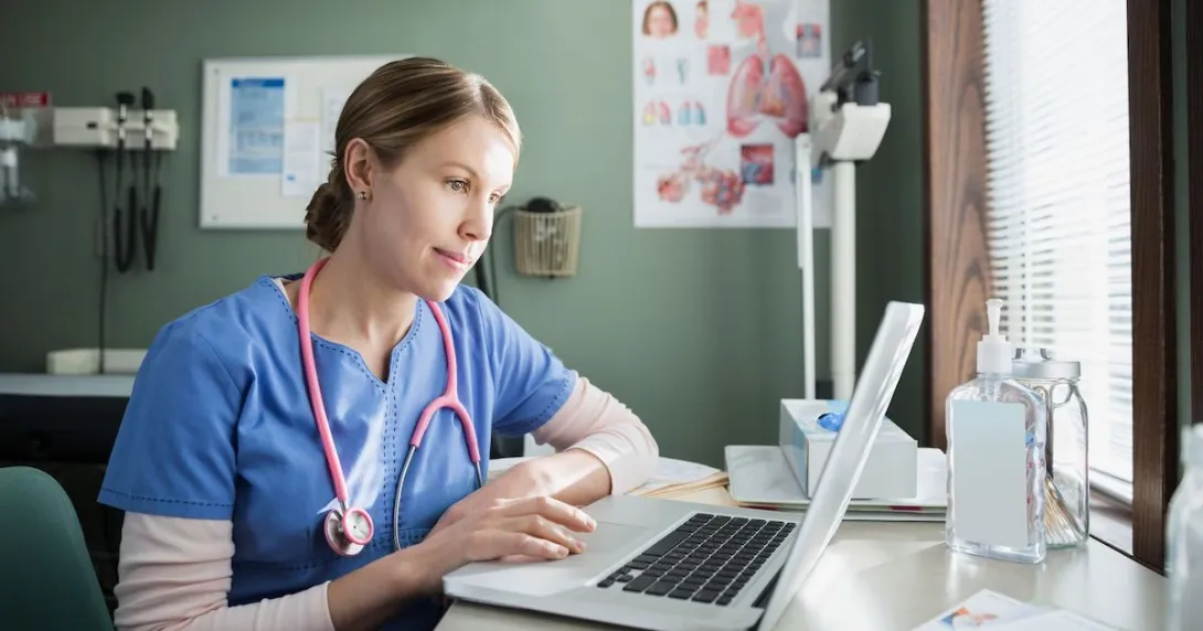 Healthcare provider in blue scrubs sitting at a desk looking at a computer