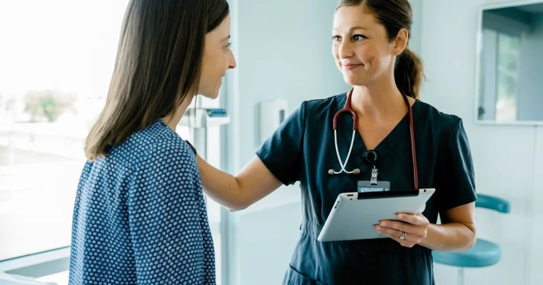A nurse holding a tablet while speaking with a patient
