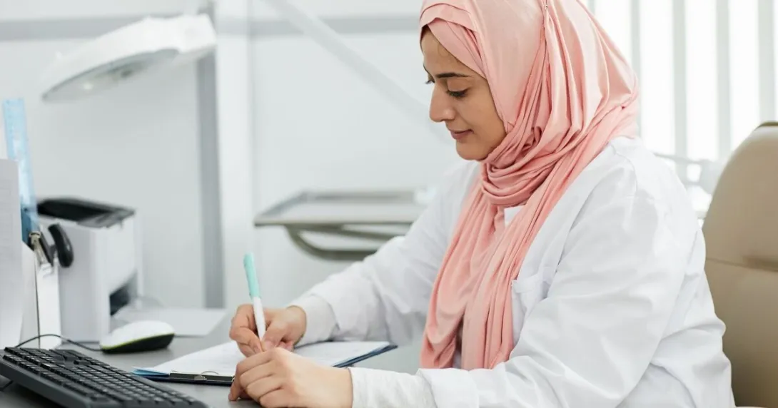 A nurse wearing hijab is filling out a patient form