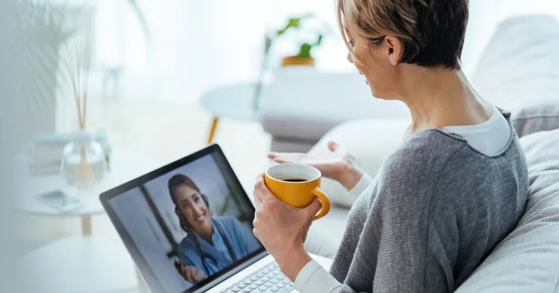 A patient holding a cup of coffee in a virtual consultation with a health professional