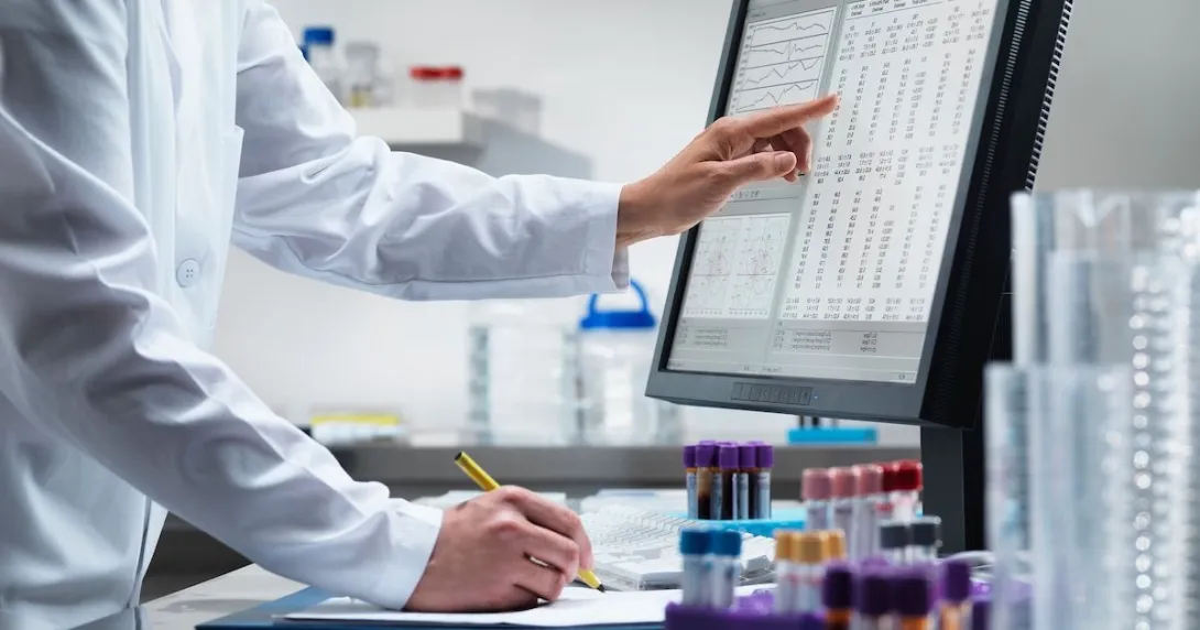 A lab researcher jotting down notes from a table flashed on a desktop computer