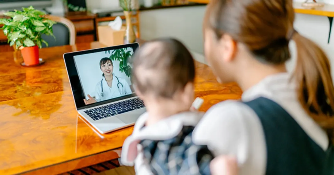 A person with a baby uses video telemedicine at a laptop
