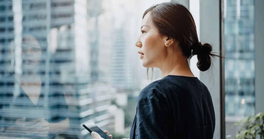 A person standing by a window using a smartphone.