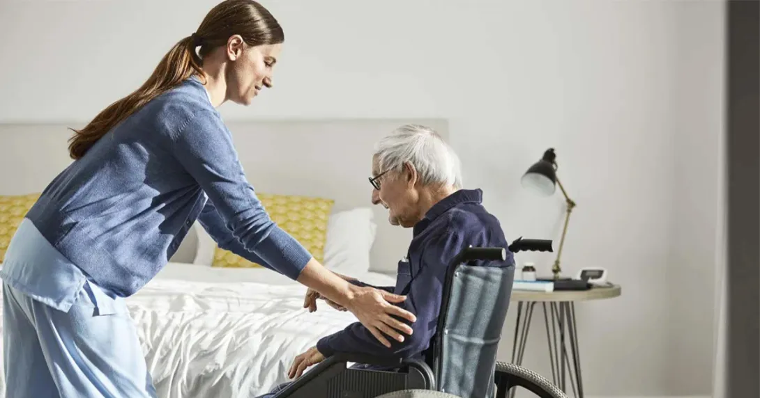 Nurse helps an elderly patient into a wheelchair at home Nurse helps an elderly patient into a wheelchair at home