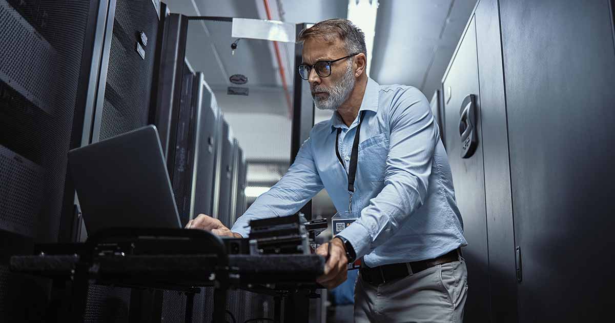 IT worker using a laptop in a server room