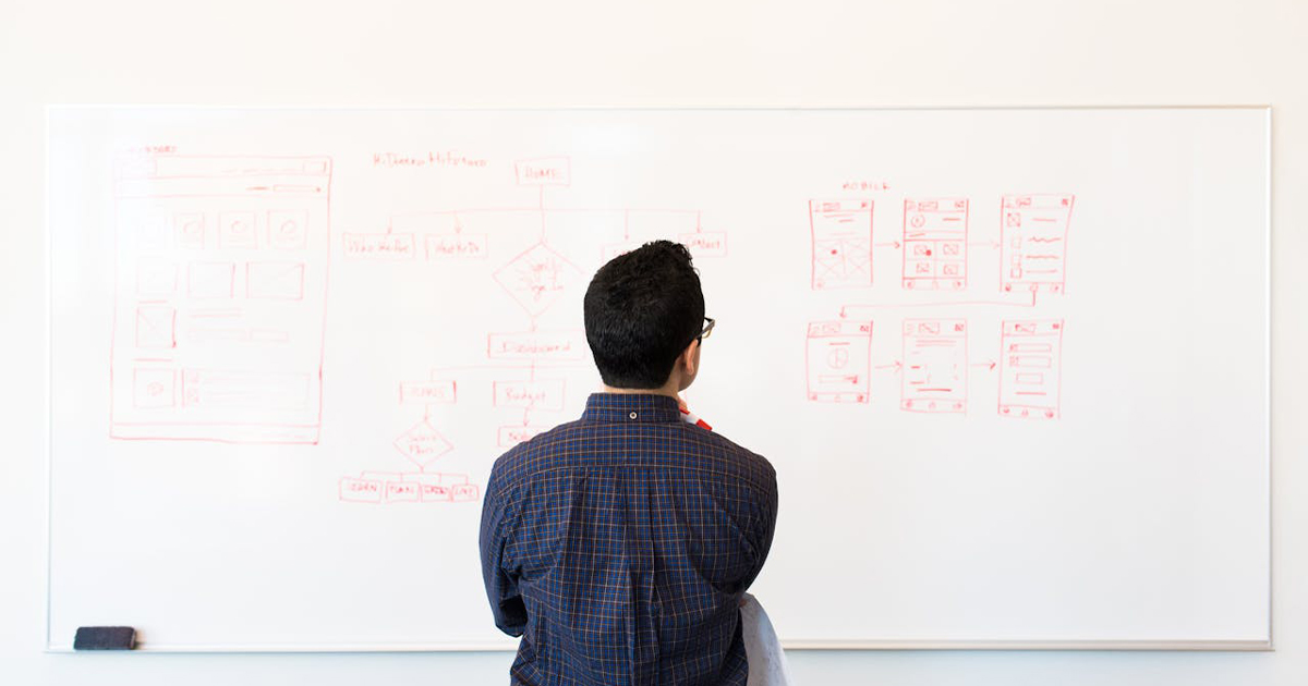 Developer faces a whiteboard looking at a tech stack diagram