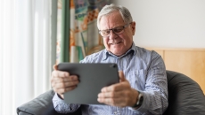 Person with gray hair and glasses surfs looking at a tablet