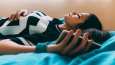 Person lying on a bed looking up at the ceiling while holding onto a cellphone