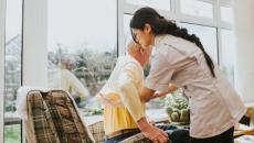 A nurse helps an older resident into her chair