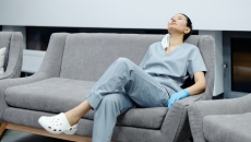 Female nurse in grey scrubs on rests on a couch with her head back