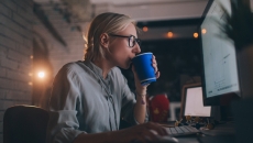 A person drinking coffee in front of a computer screen