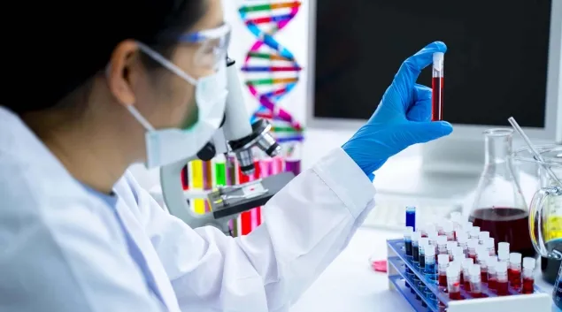 Masked healthcare worker holding vial of blood in lab