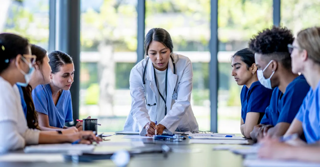 Doctor pointing out item on table to group of sitting healthcare workers Doctor pointing out item on table to group of sitting healthcare workers