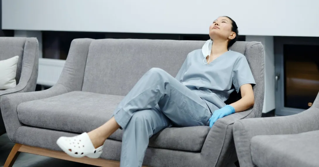 Female nurse in grey scrubs on rests on a couch with her head back Female nurse in grey scrubs on rests on a couch with her head back