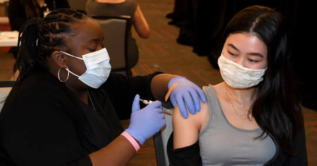 A person gets vaccinated by another, both wearing masks